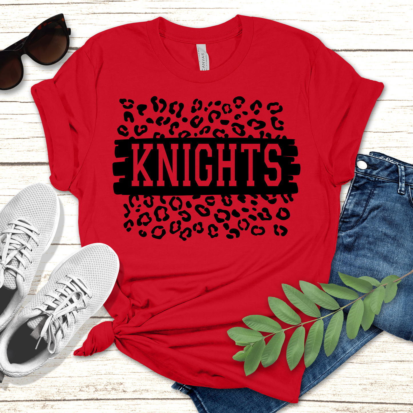 Red t-shirt with 'KNIGHTS' design on a wooden surface with shoes and jeans. Knights School Spirit Shirt - Knights Leopard - School Pride Graphic T-Shirt