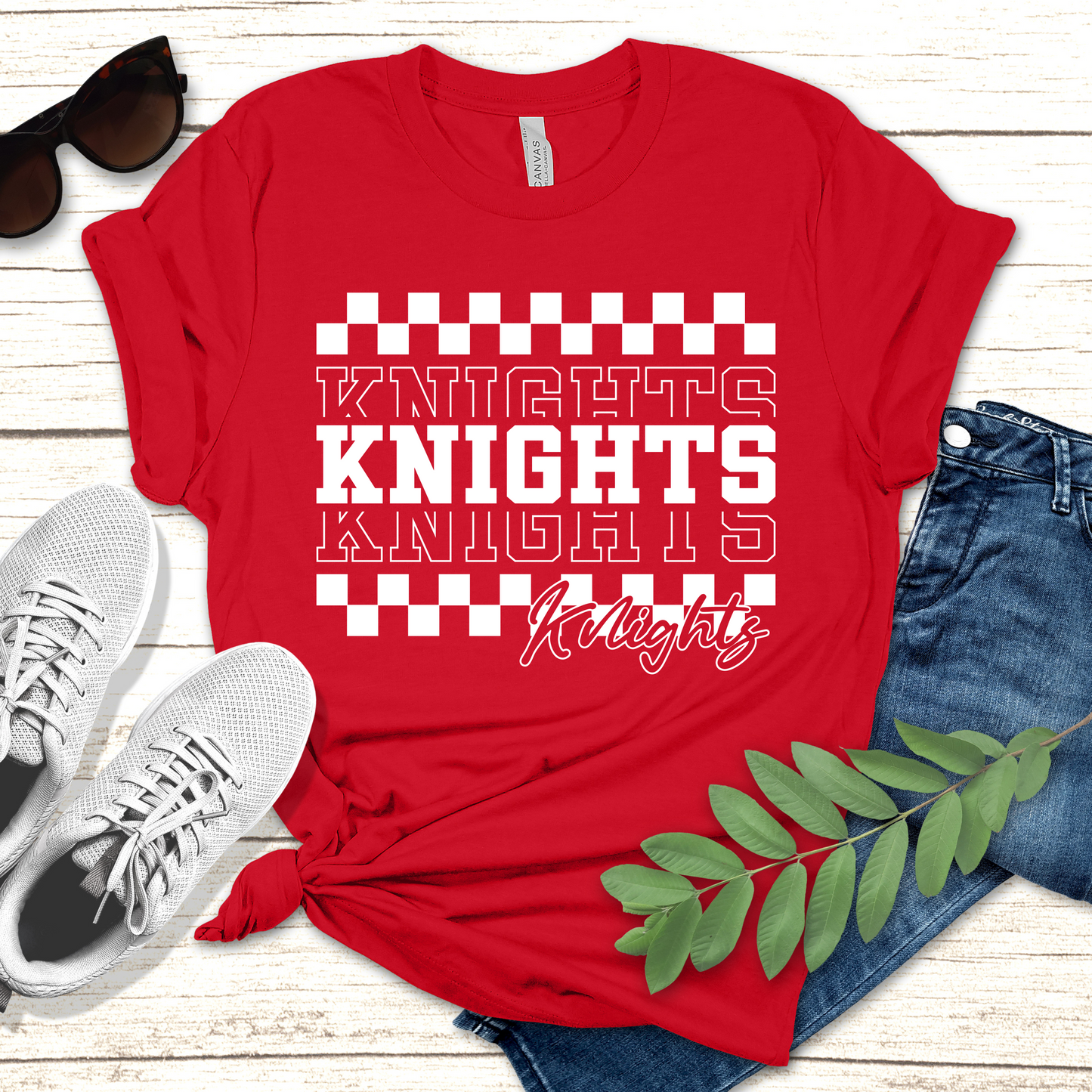 Red t-shirt with 'Knights' text, sunglasses, white sneakers, and jeans on a wooden surface. Knights School Spirit Shirt - Knights Checkered - School Pride T-Shirt