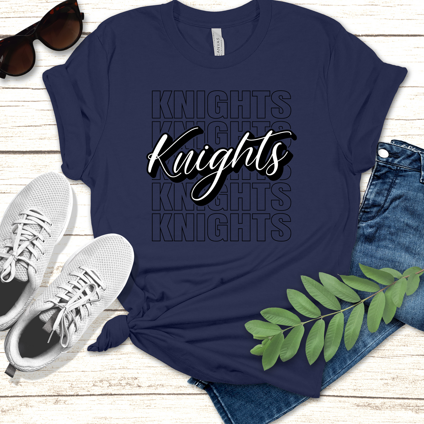 Navy blue t-shirt with 'Knights' text, sunglasses, sneakers, and jeans on a wooden surface. Knights School Spirit Shirt - Knights Cursive Stacked - School Pride T-Shirt
