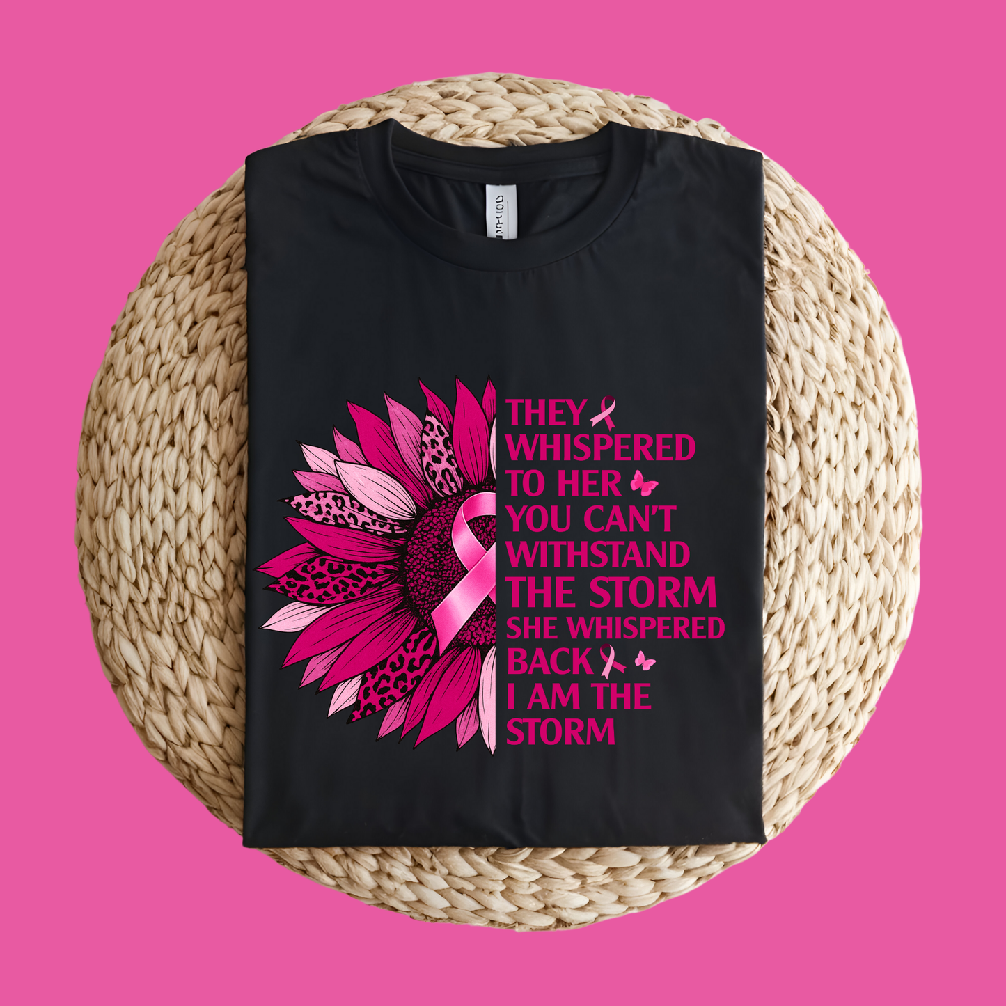 Black t-shirt with pink floral design and text on a woven mat with a pink background