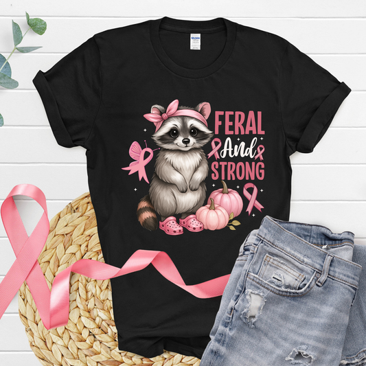 Black t-shirt with a raccoon graphic and pink text on a white wooden background Pink Ribbon Tee: Feral and Strong - Supportive Awareness T-shirt