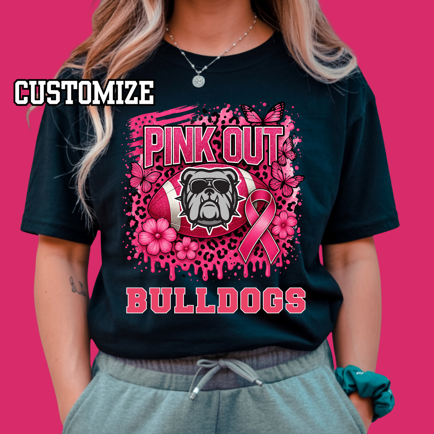 Person wearing a black t-shirt with pink 'Pink Out Bulldogs' design on a pink background Custom Pink Out Football Tee - Custom Pink Out Mascot T-Shirt