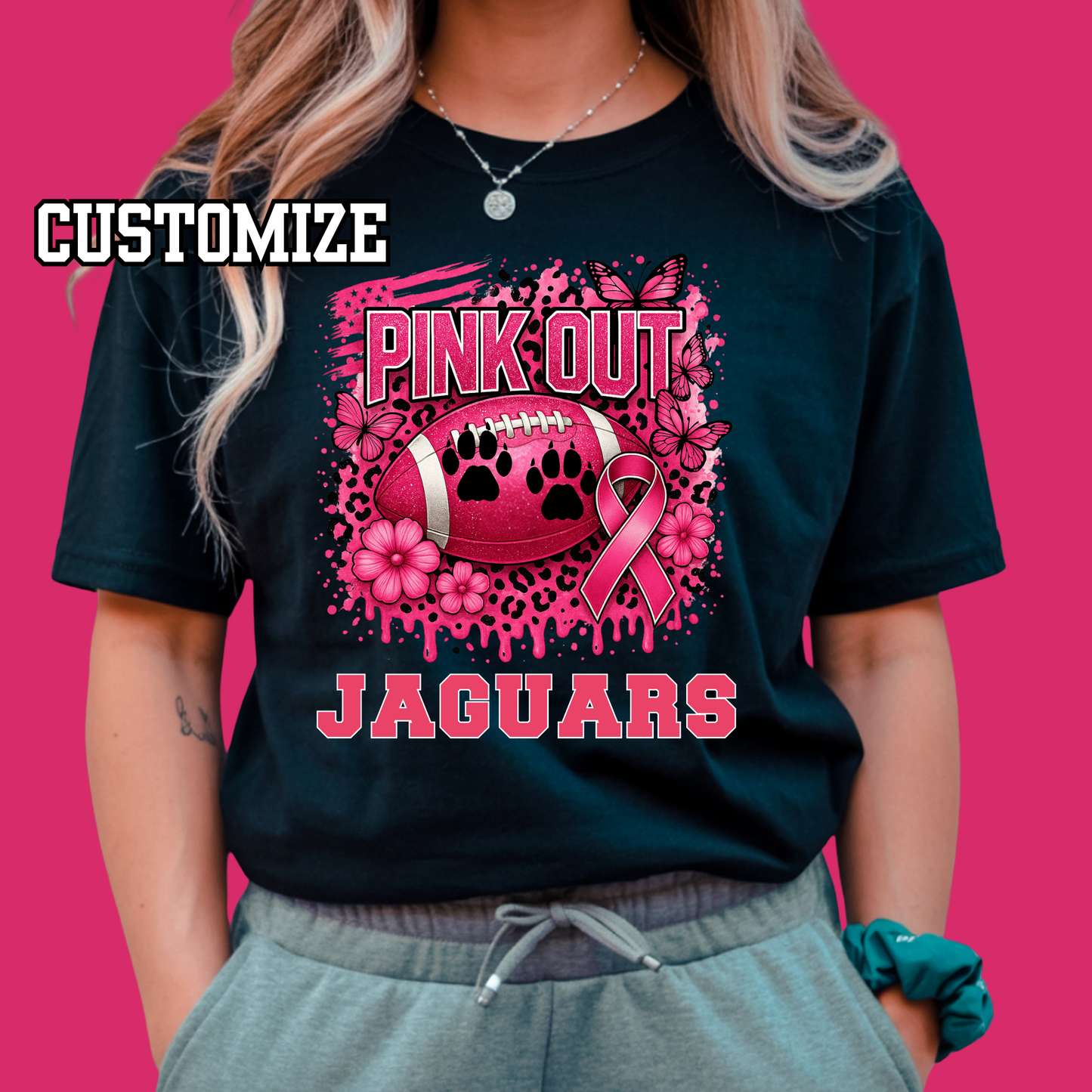 Person wearing a black t-shirt with pink 'Pink Out Jaguars' design on a pink background Custom Pink Out Football Tee - Custom Pink Out Mascot T-Shirt