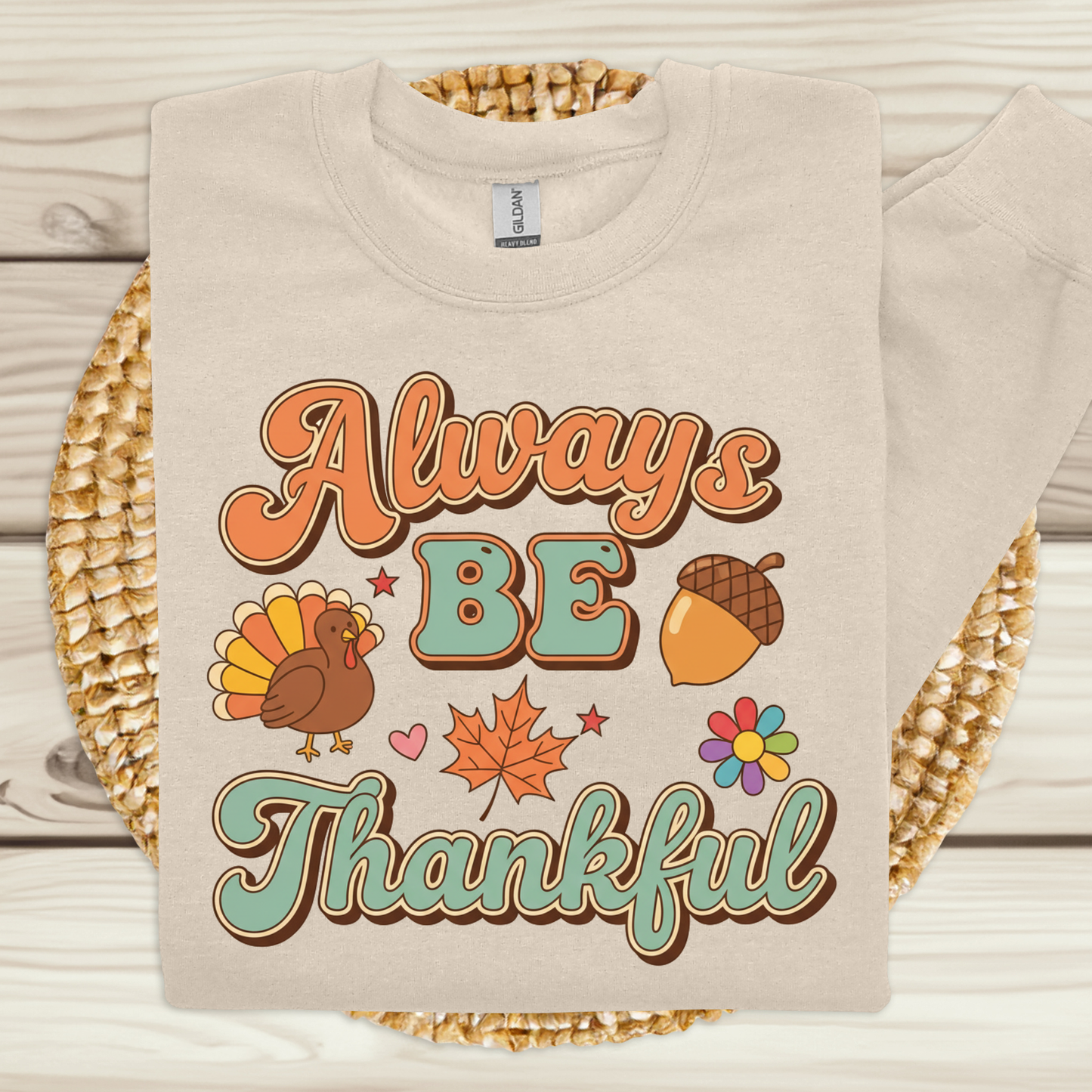 Beige sweatshirt with 'Always Be Thankful' text and Thanksgiving graphics on a wooden surface. Retro Thanksgiving Sweatshirt "Always Be Thankful" Fall Harvest Crewneck Sweater