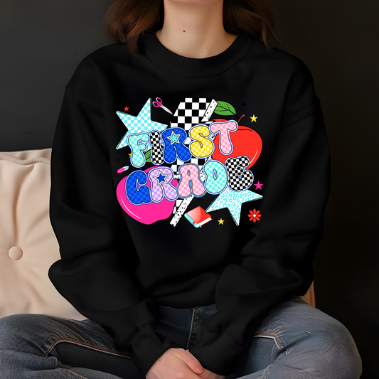 A person wearing a black crewneck sweatshirt with a colorful retro-style graphic that reads 'FIRST CRIO' in pastel bubble letters over a pink heart, star, checkered flag, and other decorative elements. The photo is cropped from the neck down, showing the person seated against a dark background with a beige cushion on the left.