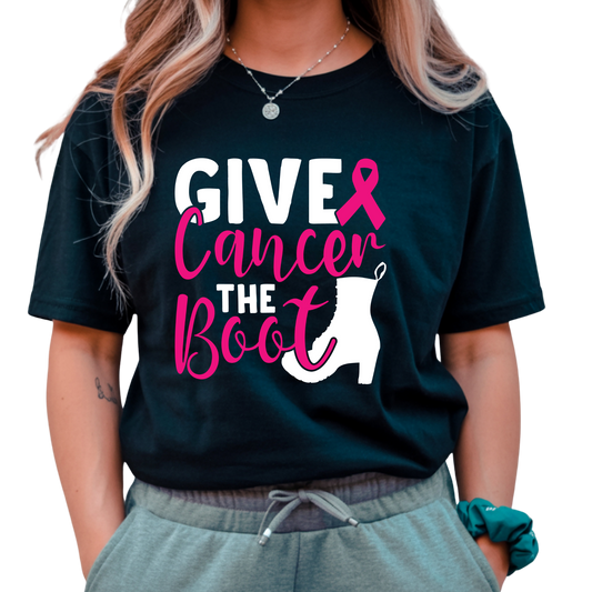 A woman wearing a black graphic t-shirt with the text 'GIVE Cancer THE Boot' in white and pink, featuring a pink ribbon and a white sock graphic. She is also wearing gray sweatpants and a teal scrunchie, set against a plain white background.