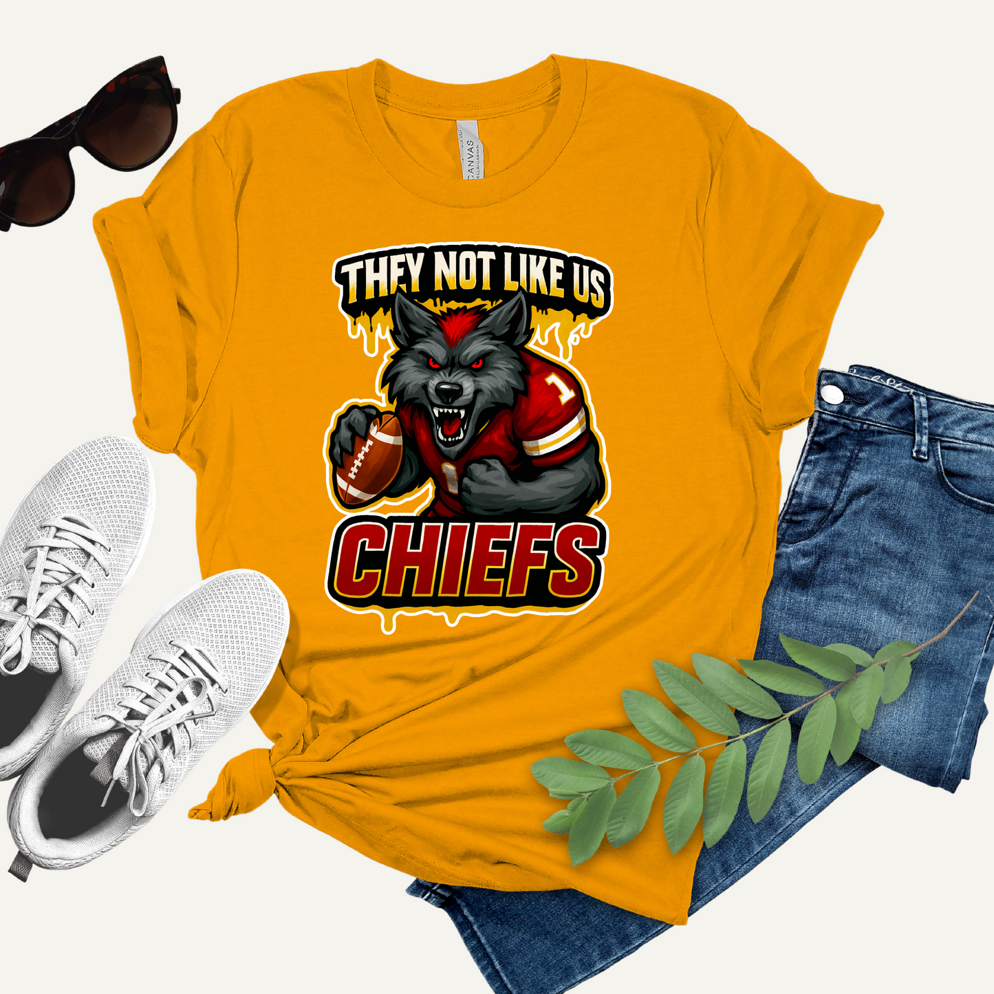 Yellow t-shirt with Chiefs graphic design, sunglasses, sneakers, and jeans on a white background Chiefs Mascot Shirt - Chiefs They Not Like Us Football Game Day Tee