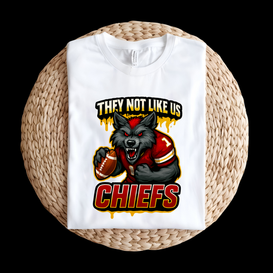 White sweatshirt with a graphic of a wolf holding a football and text 'THEY NOT LIKE US CHIEFS' on a woven surface. Chiefs Mascot Shirt - Chiefs They Not Like Us Football Game Day Tee