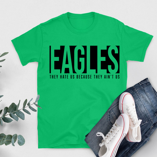 Green t-shirt with black text 'EAGLES THEY HATE US BECAUSE THEY AIN'T US' on a white background with jeans and sneakers. Eagles School Mascot Shirt - Eagles Game Day Cool School Spirit Tee