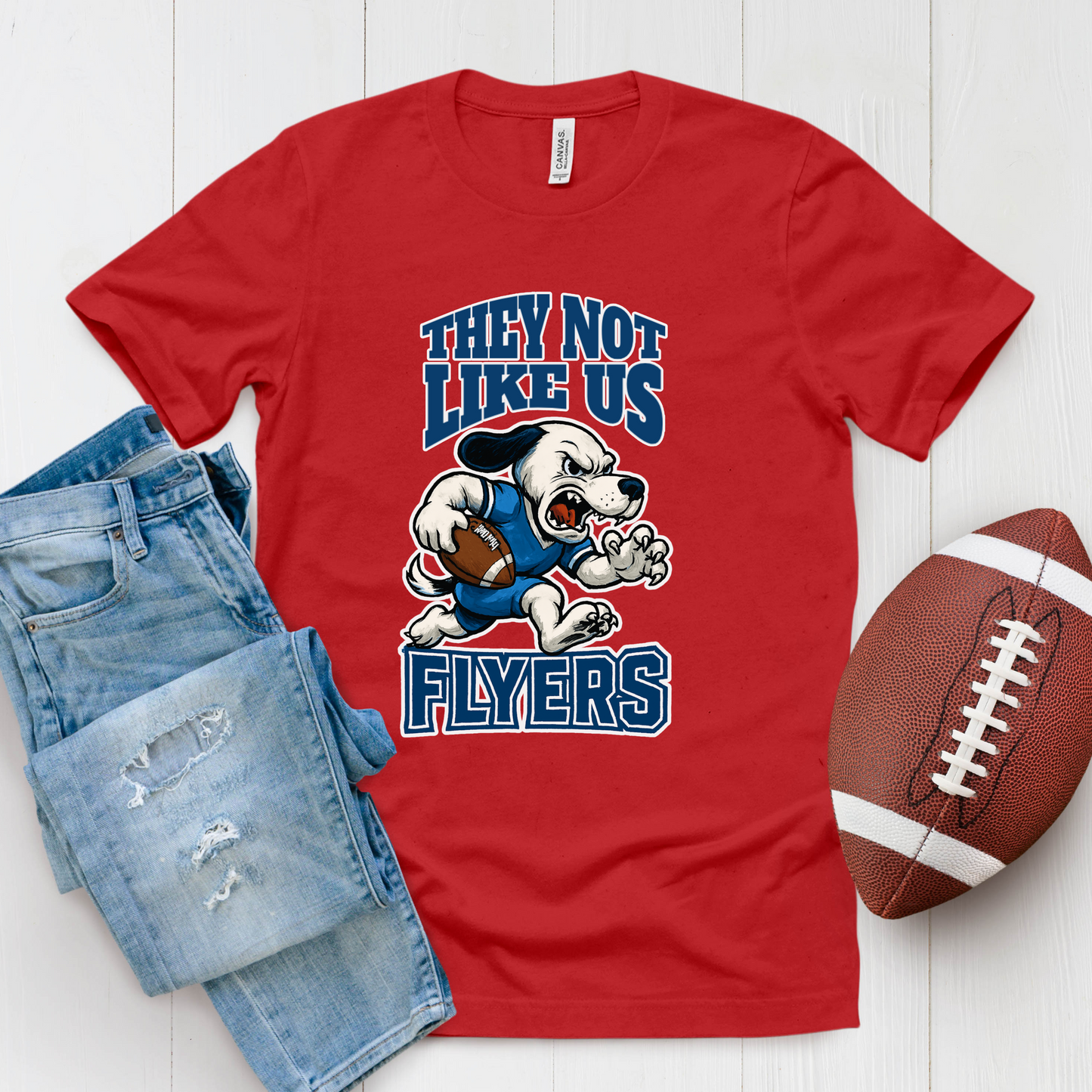Red t-shirt with 'Flyers' graphic, blue jeans, and football on a white background Flyers Mascot T-Shirt: "They Not Like Us" Flyers Game Day Graphic Tee