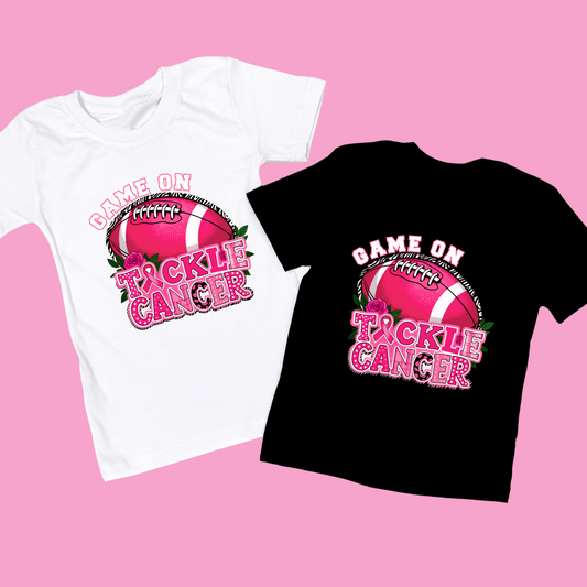 White and black t-shirts with 'Game On Tackle Cancer' design on a pink background Pink Out Football T-Shirt: Game On Tackle Awareness Support Tee
