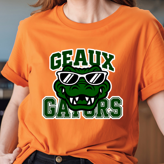 Person wearing an orange t-shirt with a green alligator graphic and text 'GEAUX GATORS'. Gators Mascot Shirt - Geaux Gators Game Day Mascot Shirt