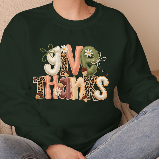 Dark green sweatshirt with 'Give Thanks' text in colorful letters, sitting on a neutral background.