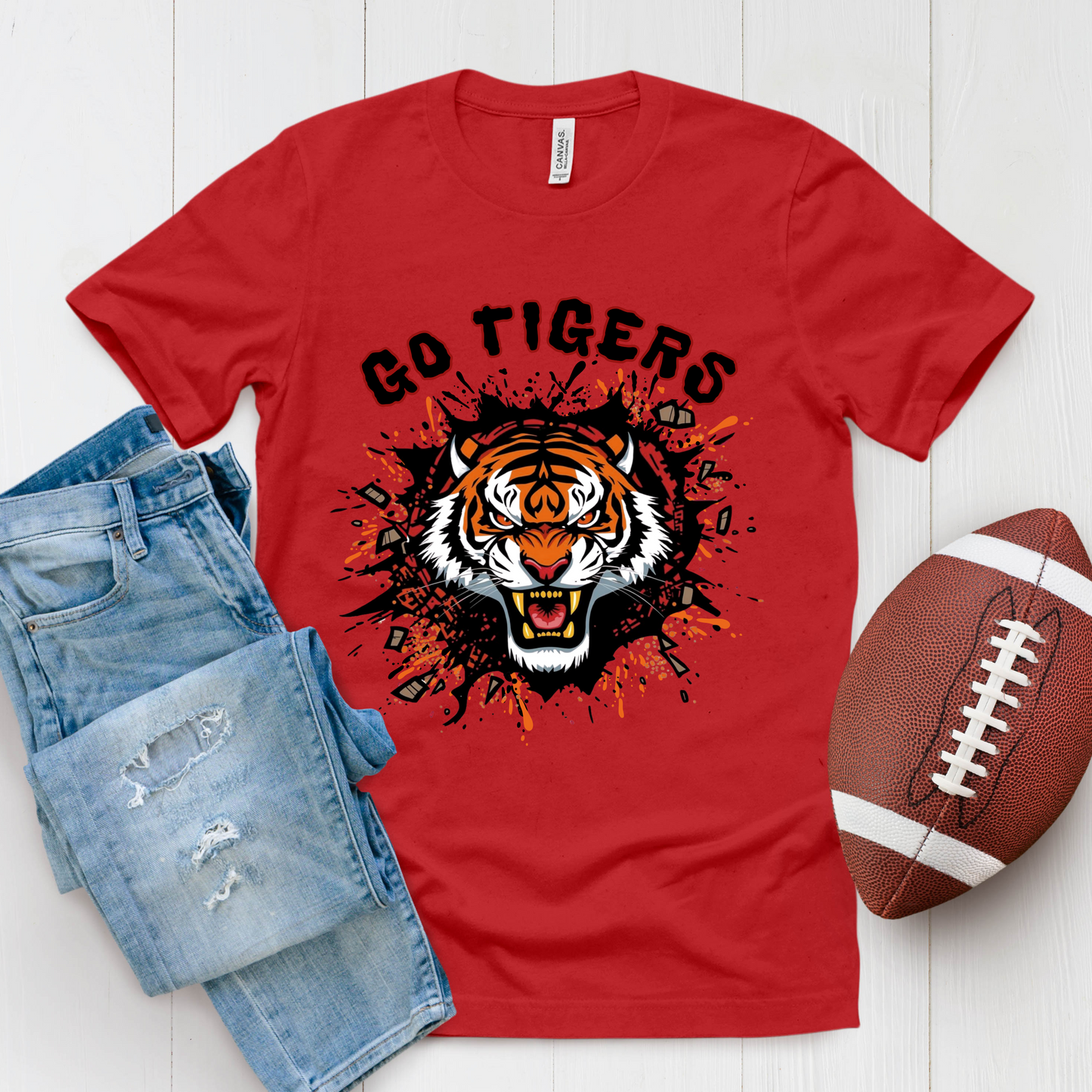 Red t-shirt with tiger graphic and 'Go Tigers' text, paired with jeans and a football on a white background. Go Tigers Bold Mascot Tee – Unleash Your School Spirit