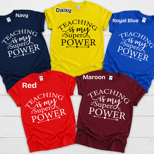 Six graphic t-shirts in different colors (Navy, Daisy yellow, Royal Blue, Red, Maroon) arranged in a circle on a white wood background. Each shirt features the text 'my students BRIGHTEN my day' in contrasting white or black lettering.