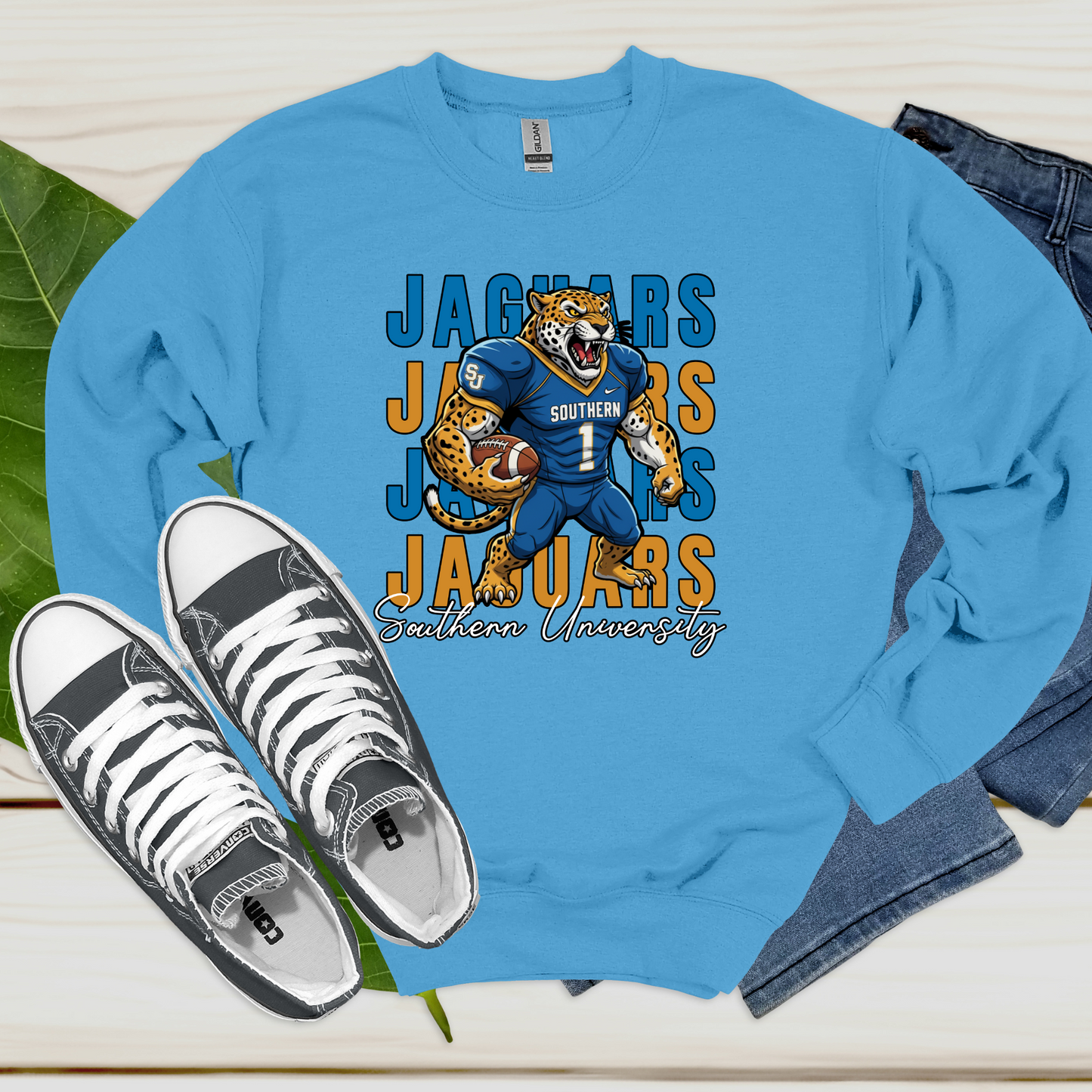 Blue sweatshirt with Jaguars graphic design, white sneakers, and jeans on a light wooden surface. Southern Jaguars Sweatshirt: HBCU Game Day Football Cozy Sweater