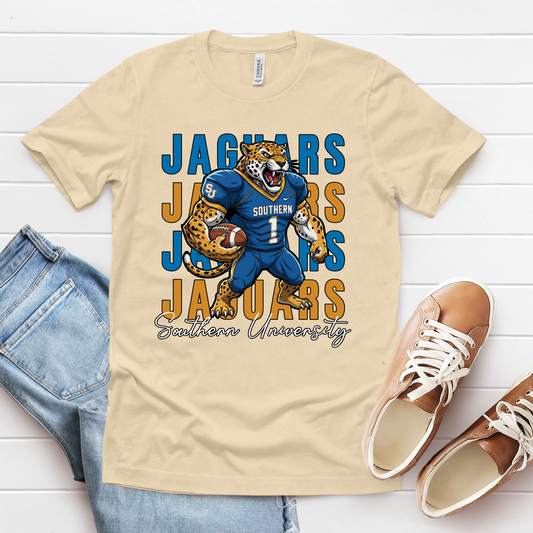 Beige t-shirt with Jaguars graphic design on a white wooden surface with jeans and shoes. Southern Jaguars T-Shirt – Southern University Game Day & Homecoming Graphic Tee