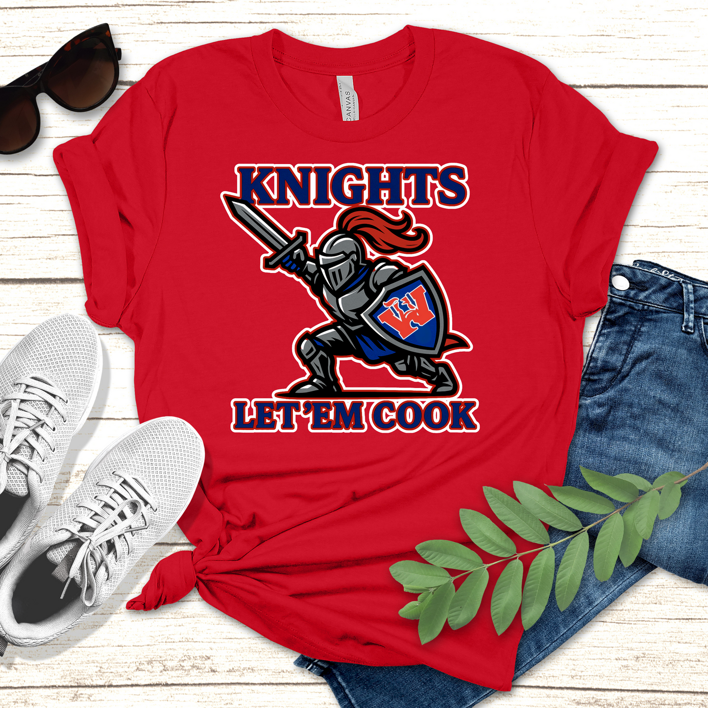 Red t-shirt with a knight graphic and text, sunglasses, white sneakers, and jeans on a wooden surface. Woodlawn Knights Shirt: "Let'em Cook" Bold Game Day T-Shirt