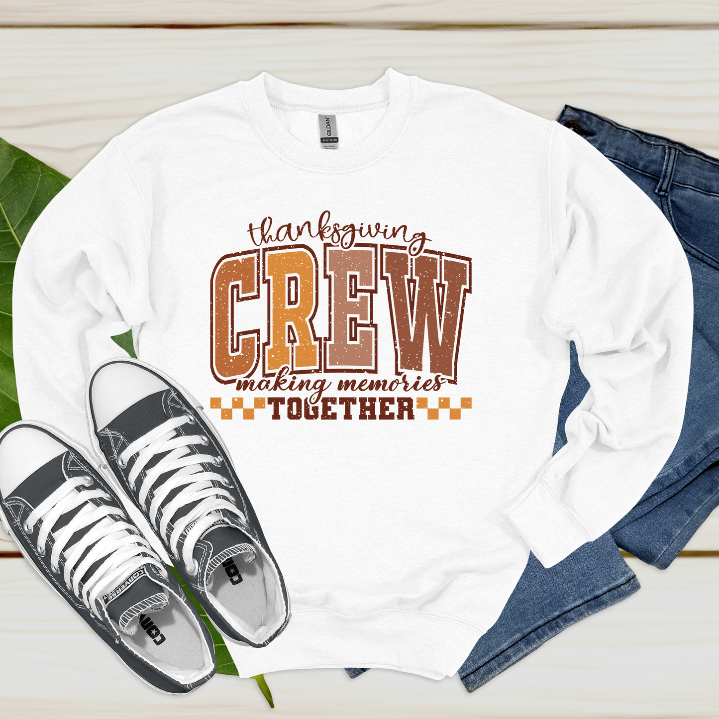 White long-sleeve shirt with 'Thanksgiving Crew making memories Together' text, paired with sneakers and jeans on a wooden surface.