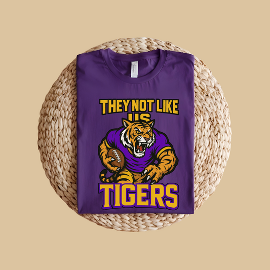 Purple t-shirt with tiger graphic and text on a woven surface Tigers Mascot Shirt - Bold Tigers They Not Like Us Game Day Spirit Tee