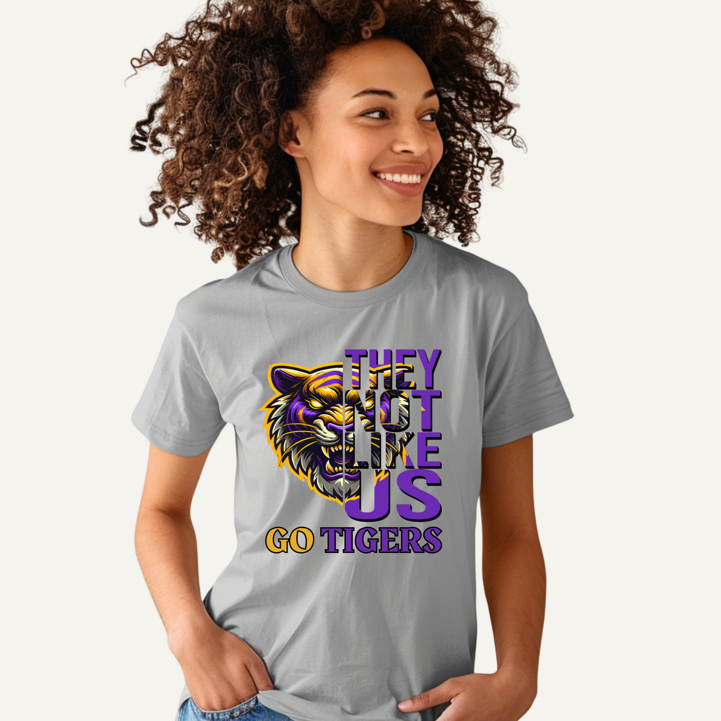 Woman wearing a gray t-shirt with a tiger graphic and text on a white background Tigers Mascot Shirt - Bold Tigers They Not Like Us Team Pride Tee