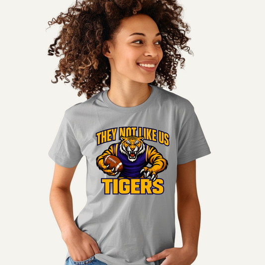 Person wearing a gray t-shirt with a tiger graphic and text on a white background Tigers Mascot T-shirt - Tigers They Not Like Us Game Day Spirit Tee Louisiana Tigers Football T-shirt - Tigers "They Not Like Us" Game Day Spirit Tee