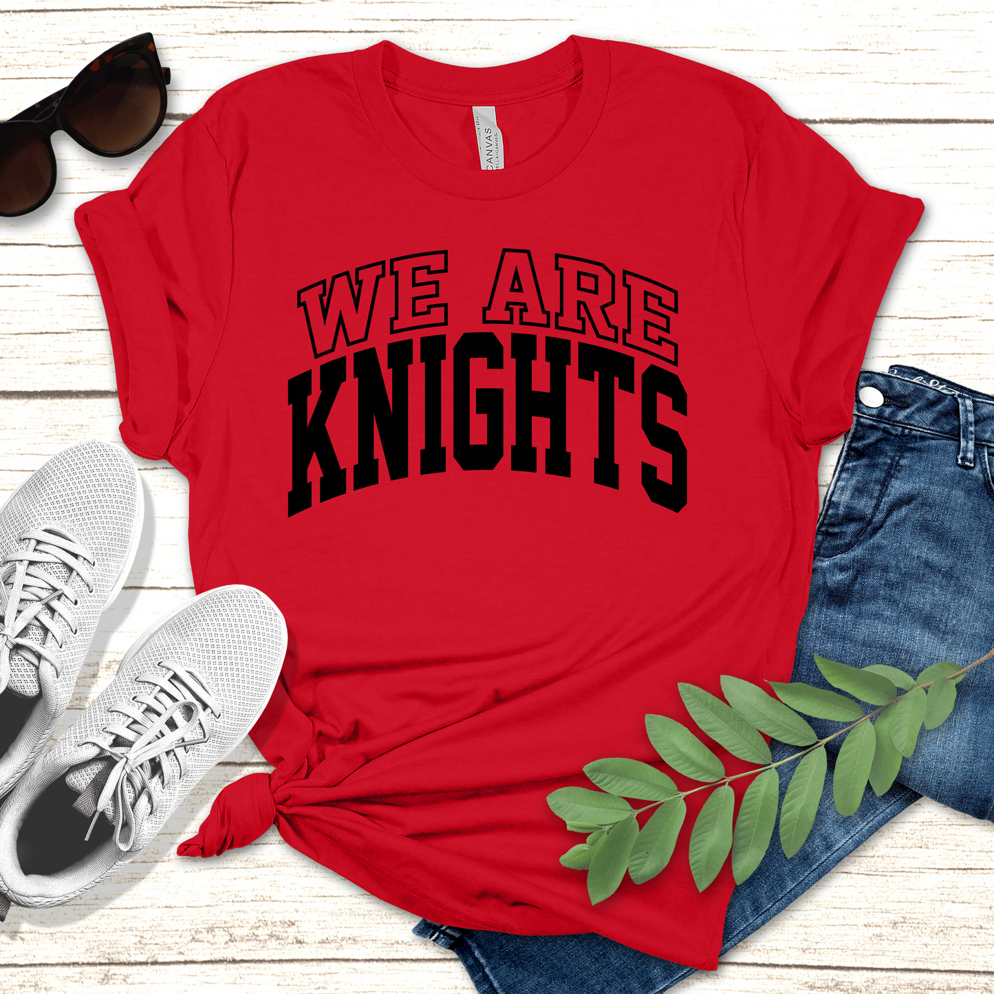 Red t-shirt with 'WE ARE KNIGHTS' text, sunglasses, white sneakers, and jeans on a wooden surface. Knights School Spirit Shirt - We Are Knights - Rep the Knights Tee