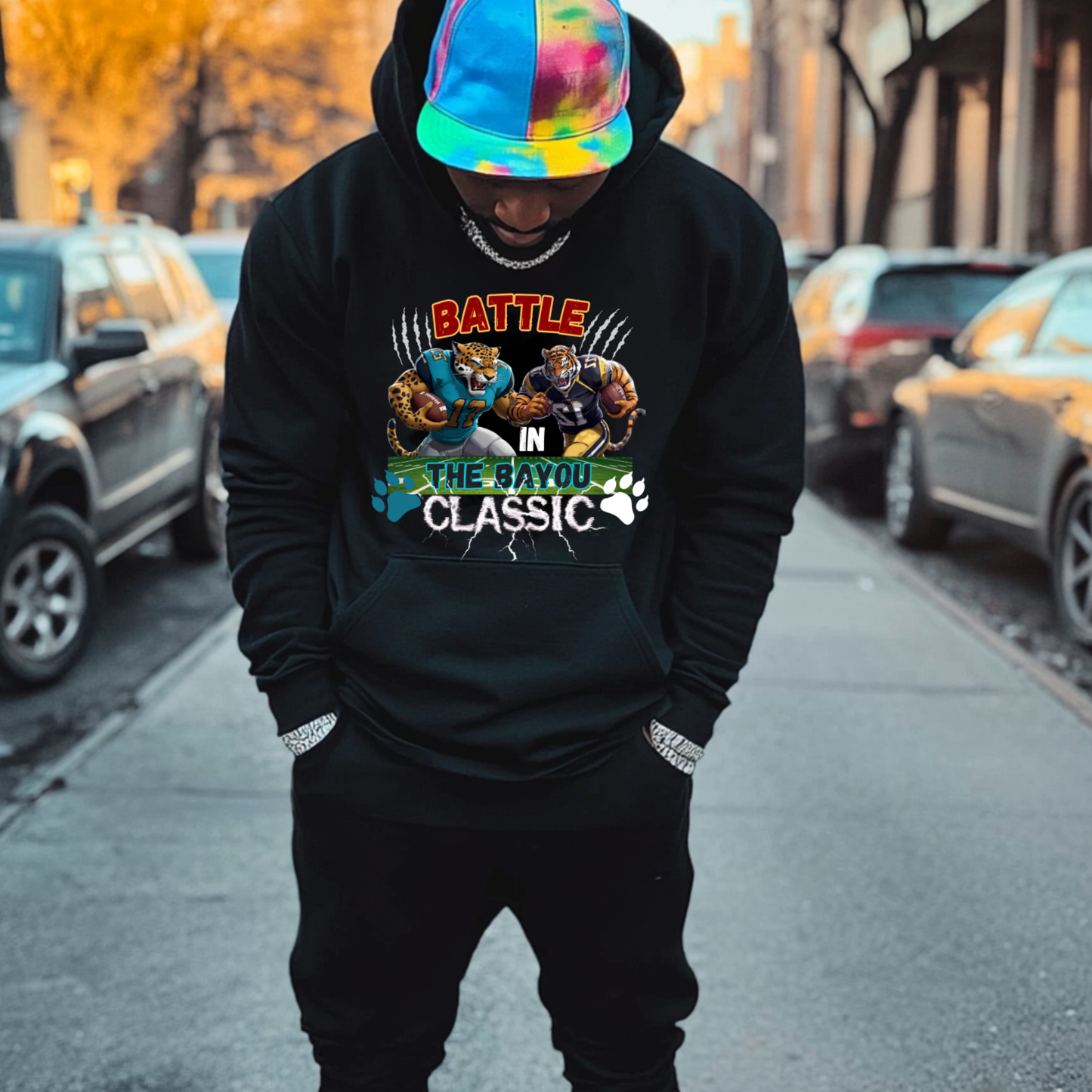 Person wearing a black hoodie with a graphic design on a city street. Bayou Classic Hoodie: Battle in the Bayou Classic Game Day Unisex Hoodie