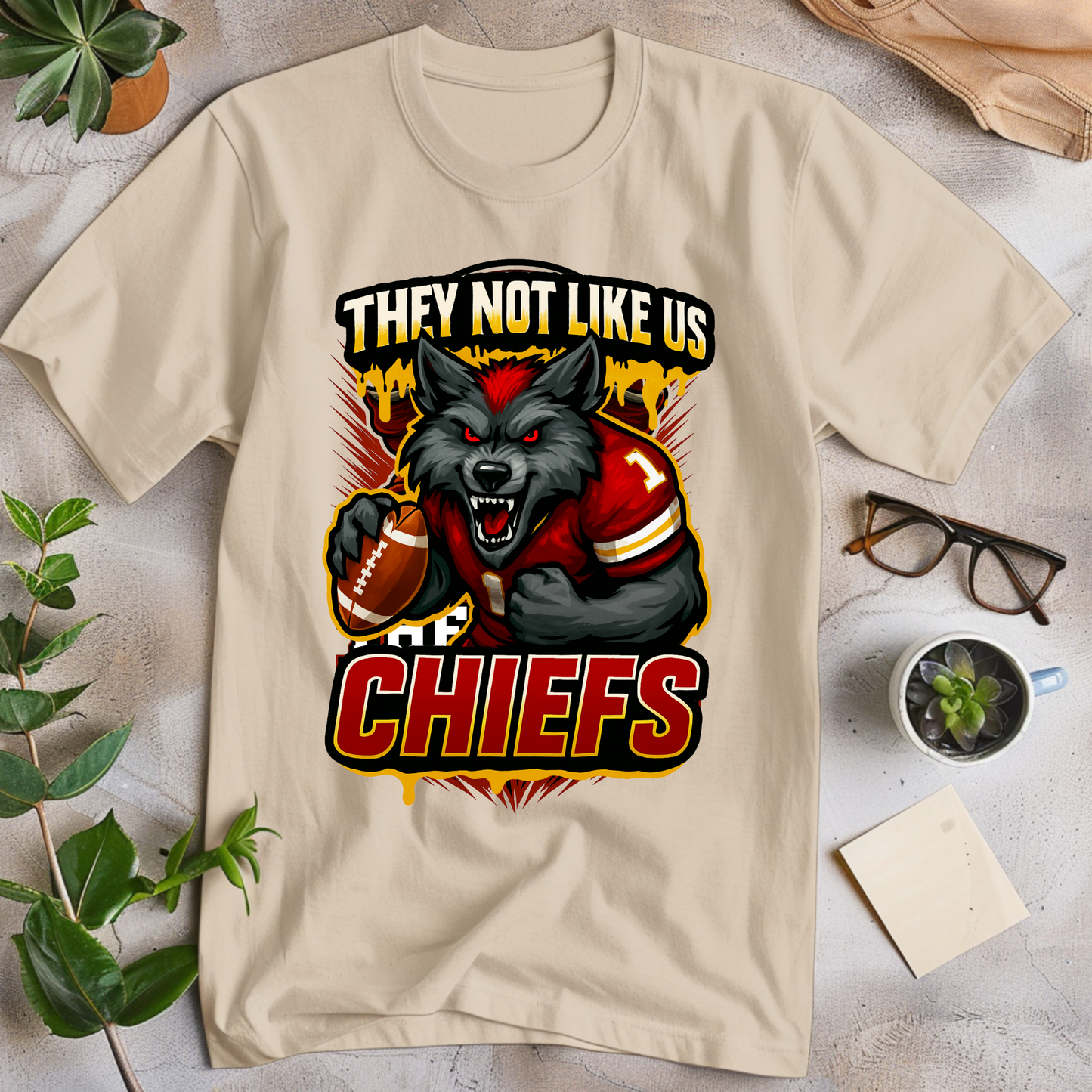Beige t-shirt with a graphic of a wolf holding a football and text 'THEY NOT LIKE US CHIEFS' on a light surface. Chiefs Mascot Shirt - Chiefs They Not Like Us Football Game Day Tee