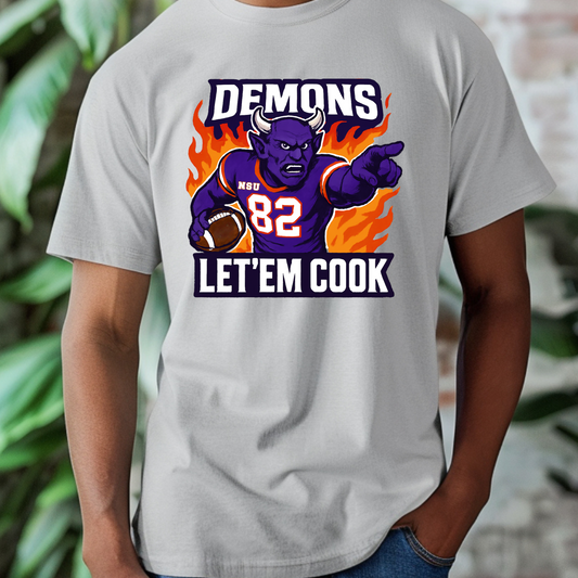 Gray t-shirt with a graphic of a demon holding a football and text 'DEMONS 82 LET'EM COOK' on a blurred background. Northwestern Demons Game Day T-Shirt - Demons "Let'em Cook" Football Tee