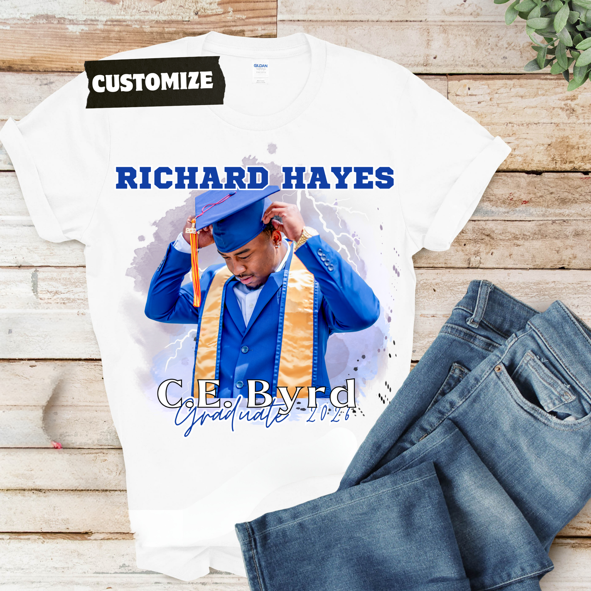 Graduation-themed t-shirt with personalized text on a wooden surface  Customizable graduation photo t-shirt featuring senior portrait, school mascot, and sports organization logos in school colors