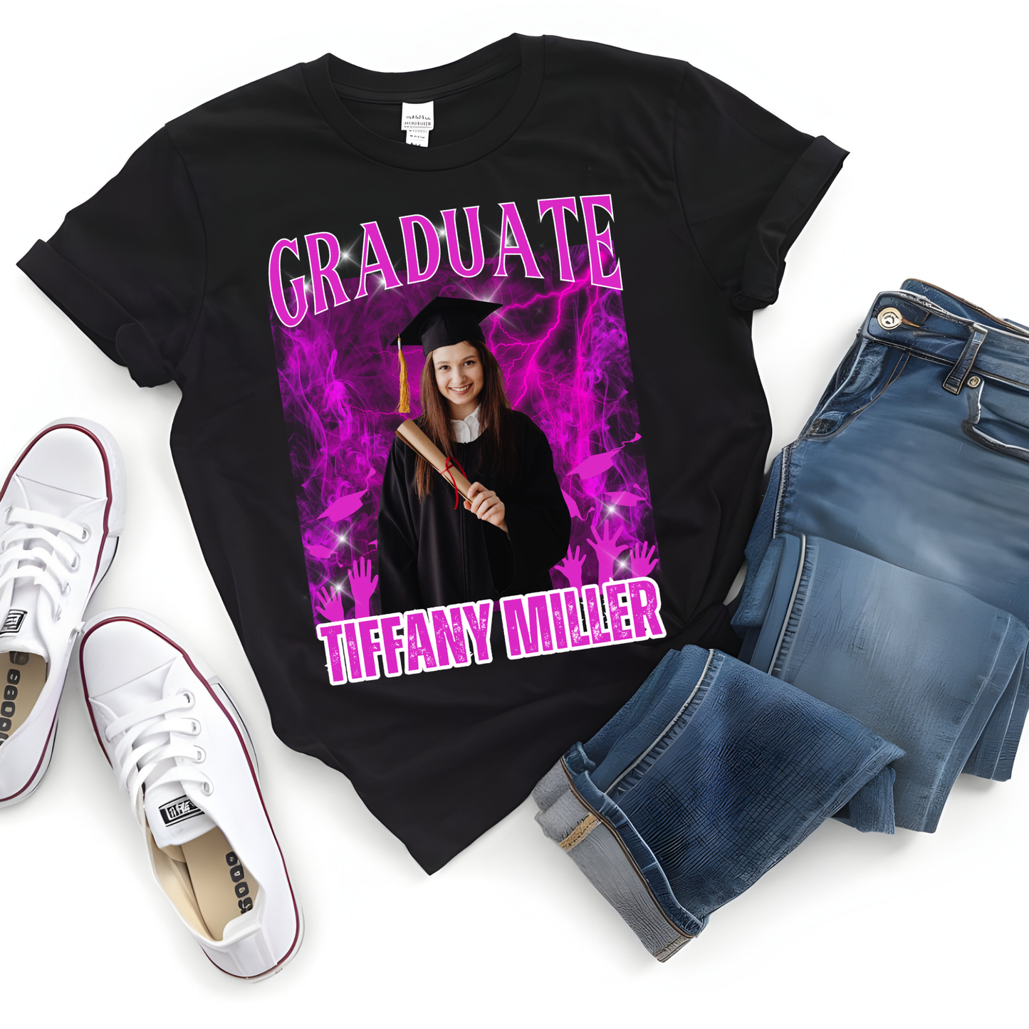 Graduation-themed t-shirt with a photo of a graduate, surrounded by pink smoke, on a black background. The shirt is displayed with jeans and white sneakers.  Customizable graduation photo t-shirt featuring senior portrait, school mascot, and sports organization logos in school colors