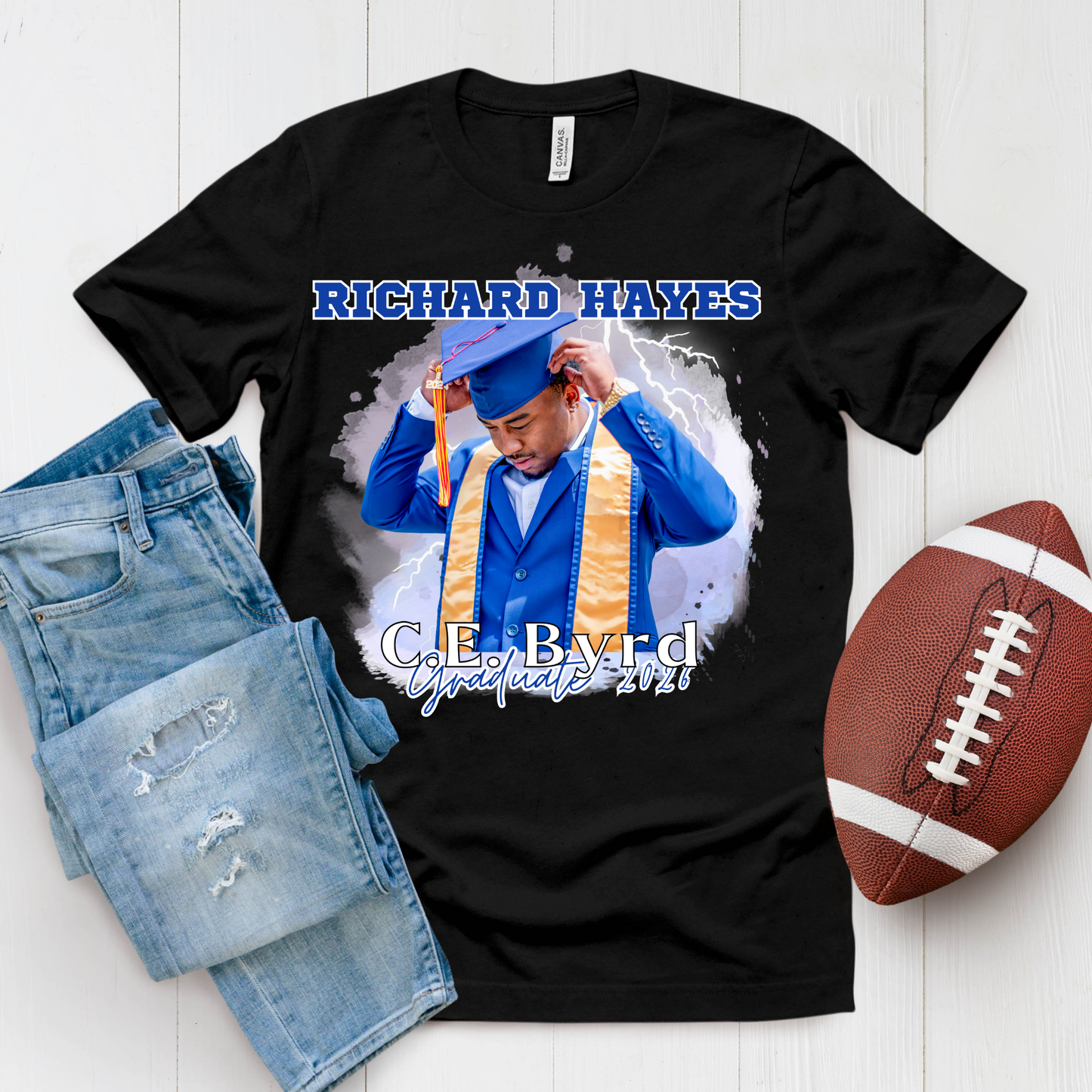 Black t-shirt with graduation design, jeans, and football on a white background  Customizable graduation photo t-shirt featuring senior portrait, school mascot, and sports organization logos in school colors