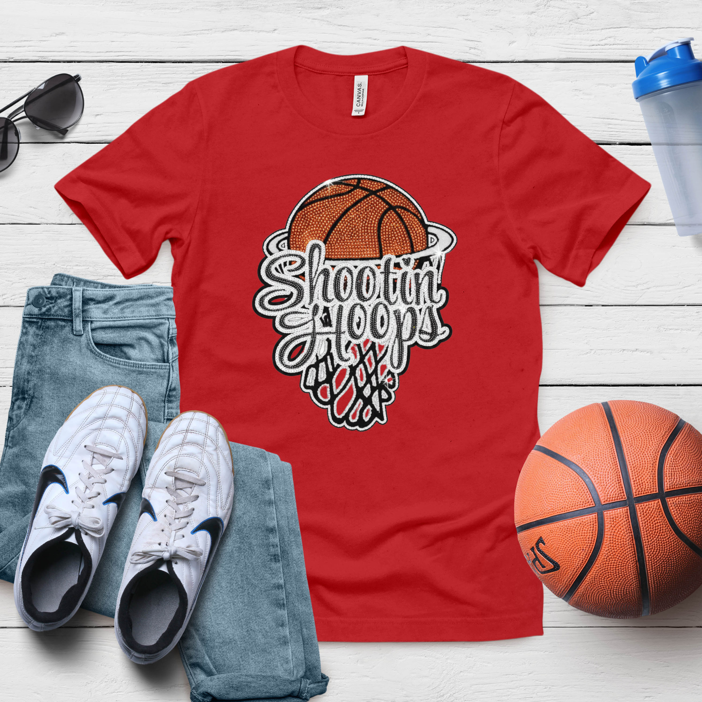 Red t-shirt with basketball graphic and text, paired with jeans, sneakers, and a basketball on a wooden surface.