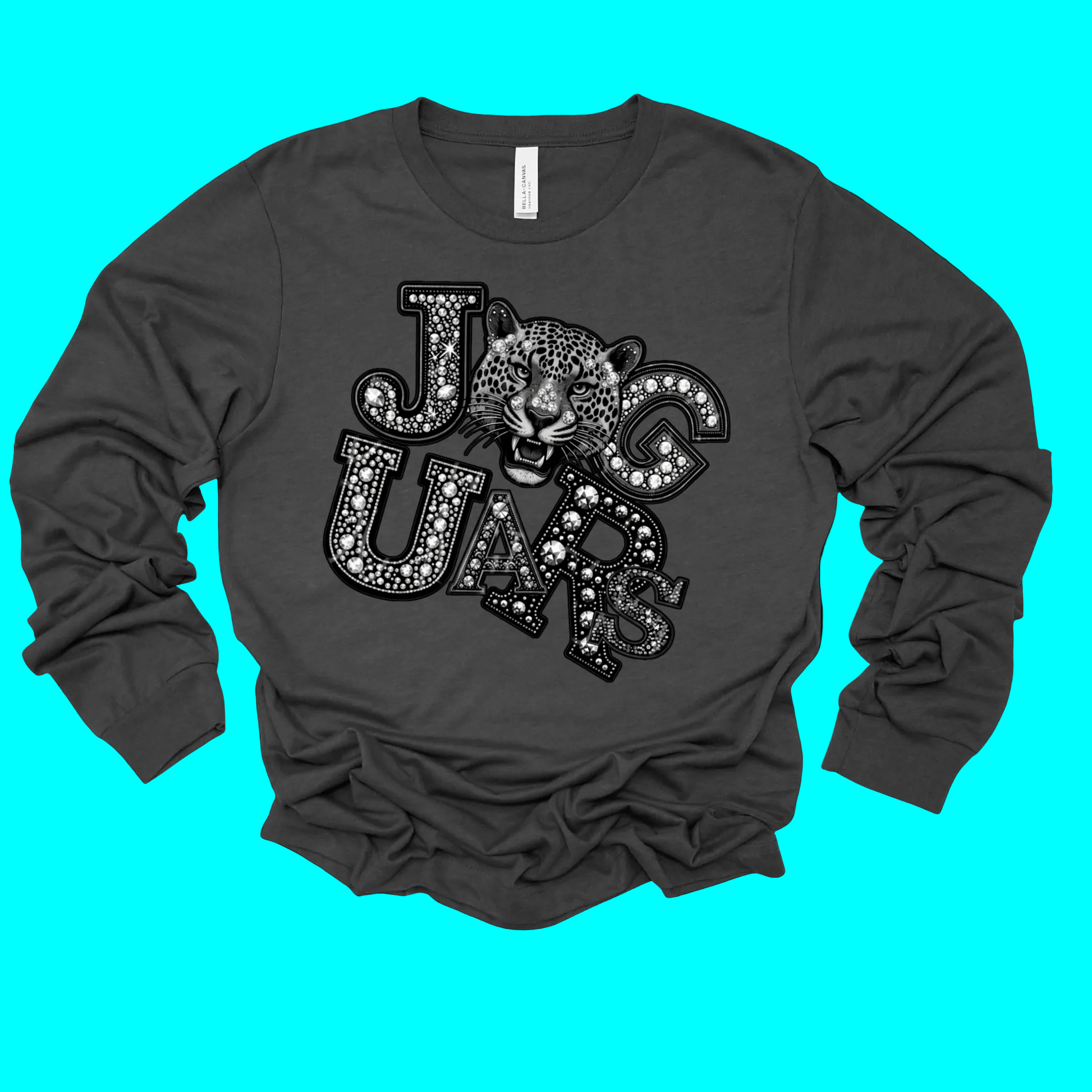 A dark gray long-sleeve t-shirt with a graphic print of the word 'JAGUARS' in a patterned font, featuring a jaguar head in the center, displayed on a solid black background.