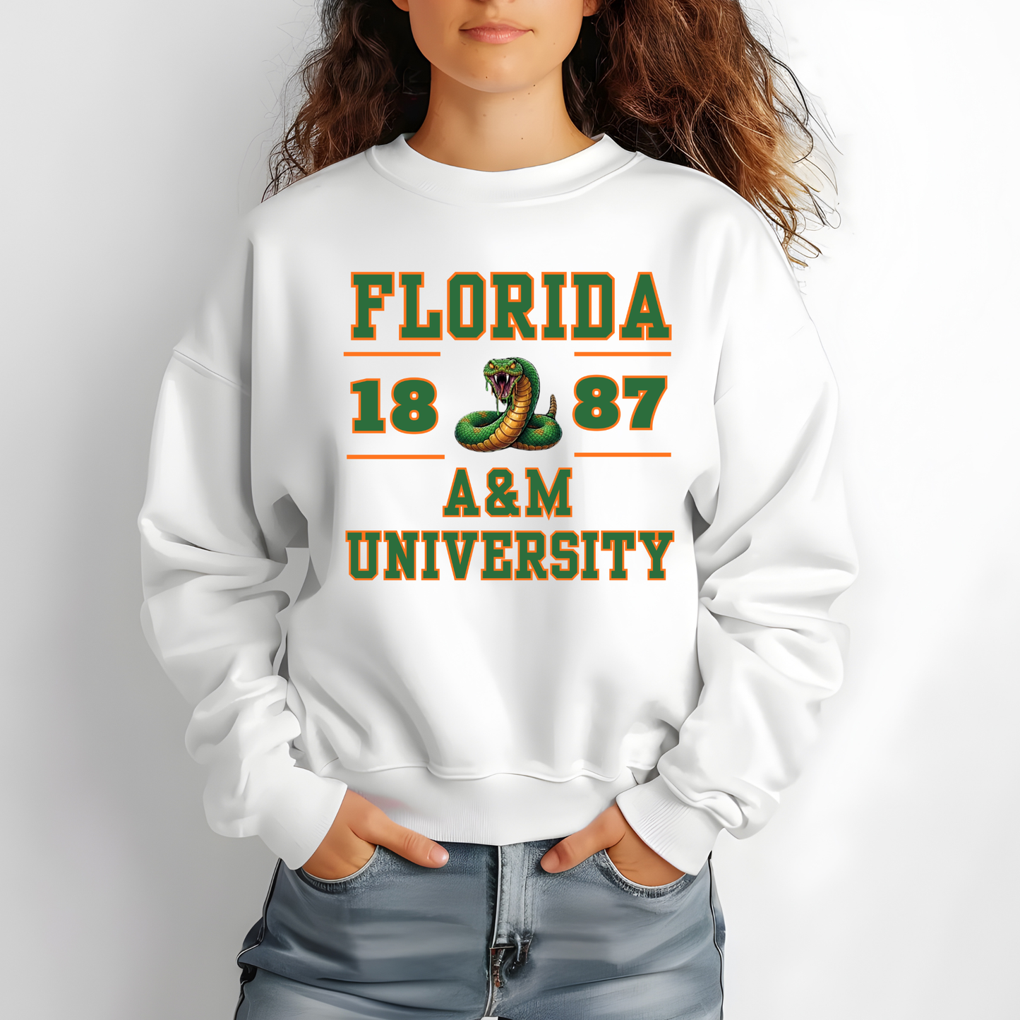 A person wearing a white crewneck sweatshirt with a green and orange graphic that reads 'FLORIDA 1887 A&M UNIVERSITY' with a snake illustration, paired with light blue jeans against a light gray background.