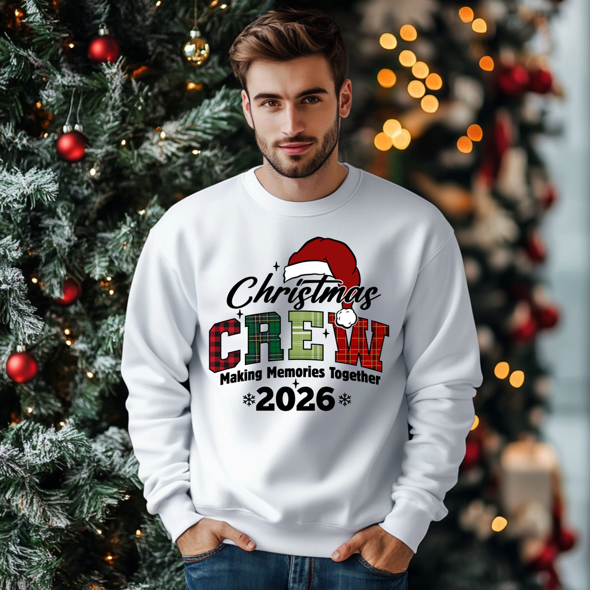 A man wearing a white crewneck sweatshirt with a 'Christmas Crew 2026' graphic, standing in front of a decorated Christmas tree with warm bokeh lights.