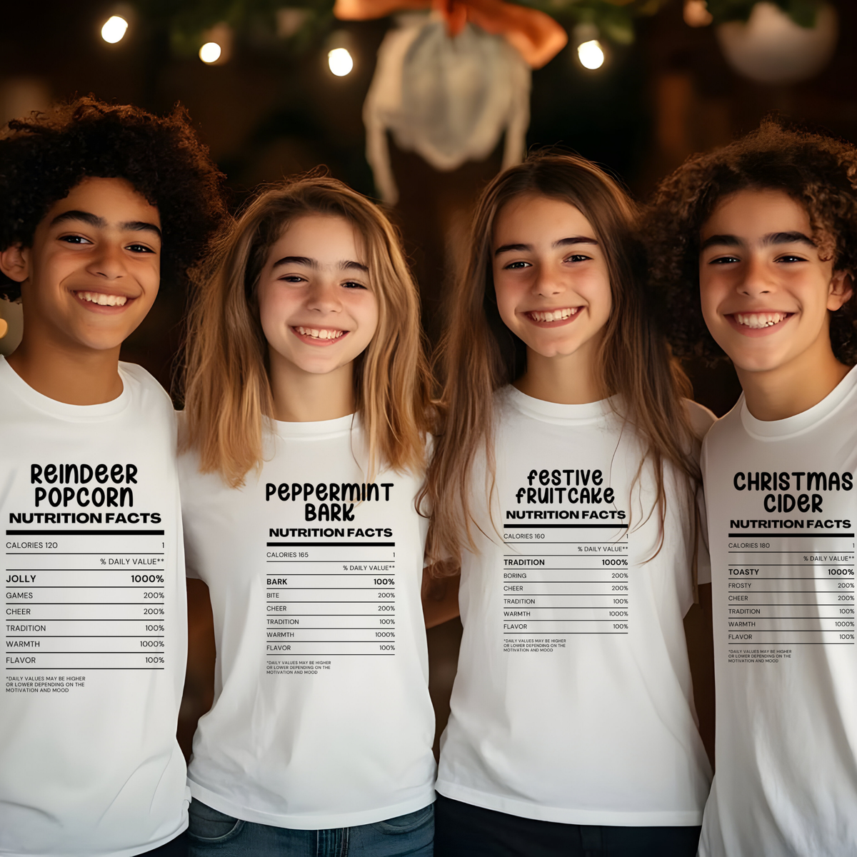 Four children standing together and smiling, each wearing a white graphic T-shirt with a black nutrition-facts label design and holiday-themed text including 'Reindeer Popcorn,' 'Peppermint Bark,' 'Festive Fruitcake,' and 'Christmas Cider.'.