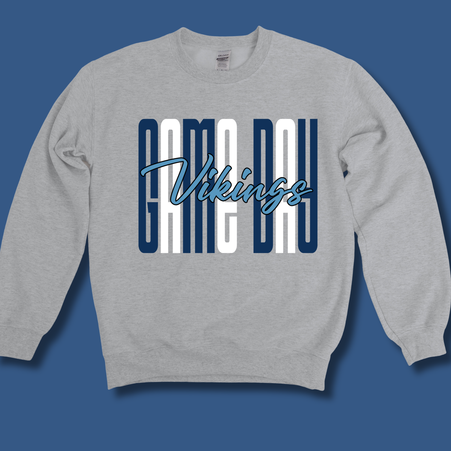 A heather gray crewneck sweatshirt featuring a 'Camo Day Vikings' graphic on the chest, displayed against a solid blue background.