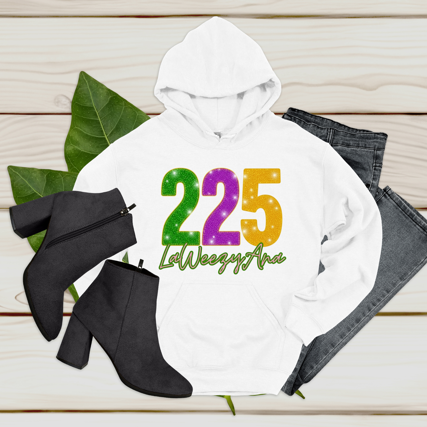 White hoodie with colorful text, black boots, and jeans on a wooden surface