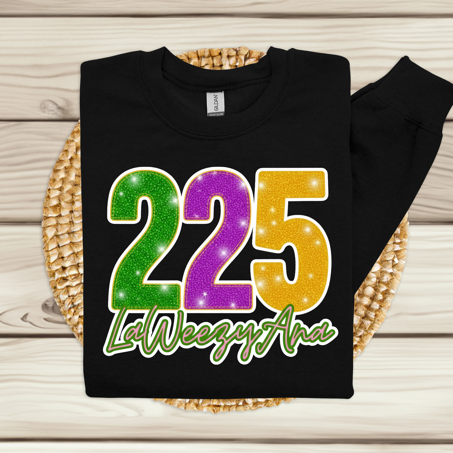 Black sweatshirt with colorful '225 LaWeezy Ana' text on a woven mat.