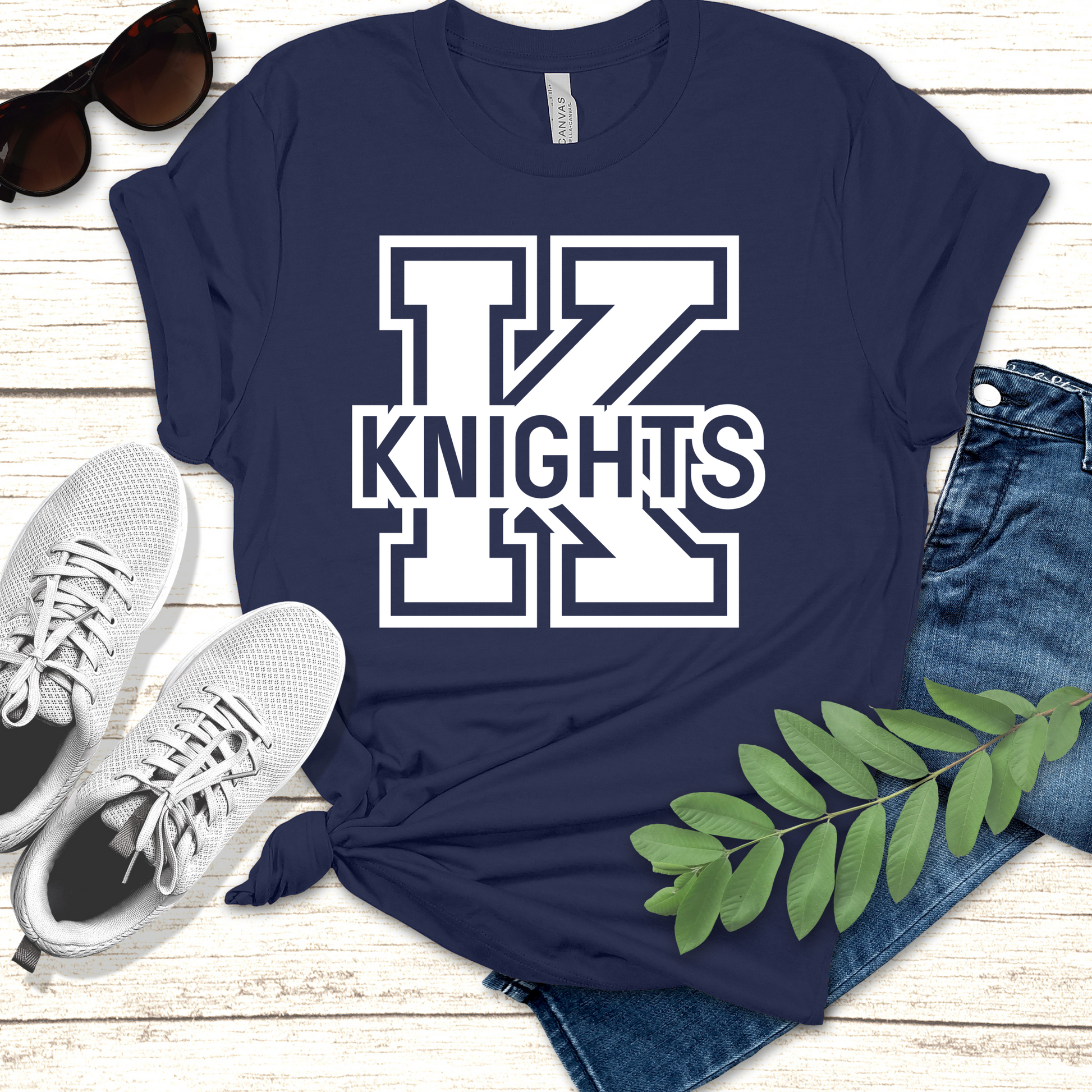 Navy blue t-shirt with 'KNIGHTS' print on a wooden surface with sneakers and sunglasses. Knights School Spirit Shirt - Knights Logo: Loud & Proud Knights