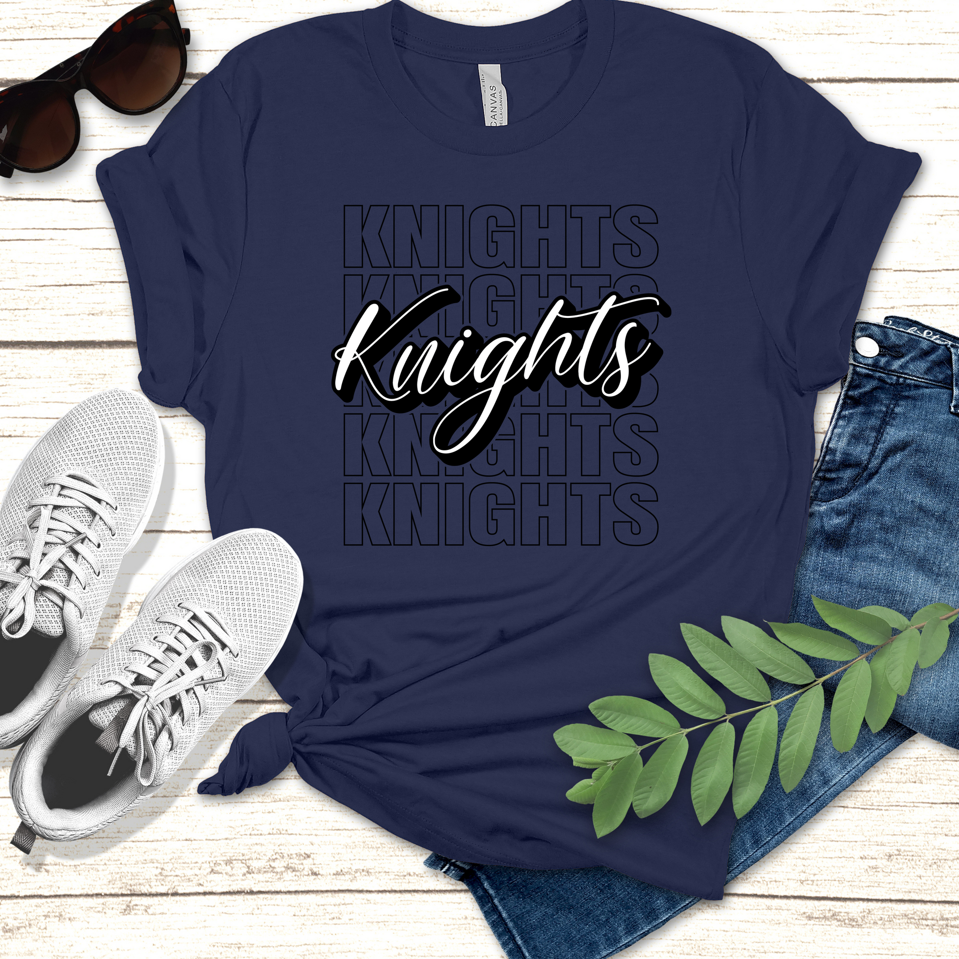 Navy blue t-shirt with 'Knights' text, sunglasses, sneakers, and jeans on a wooden surface. Knights School Spirit Shirt - Knights Cursive Stacked - School Pride T-Shirt