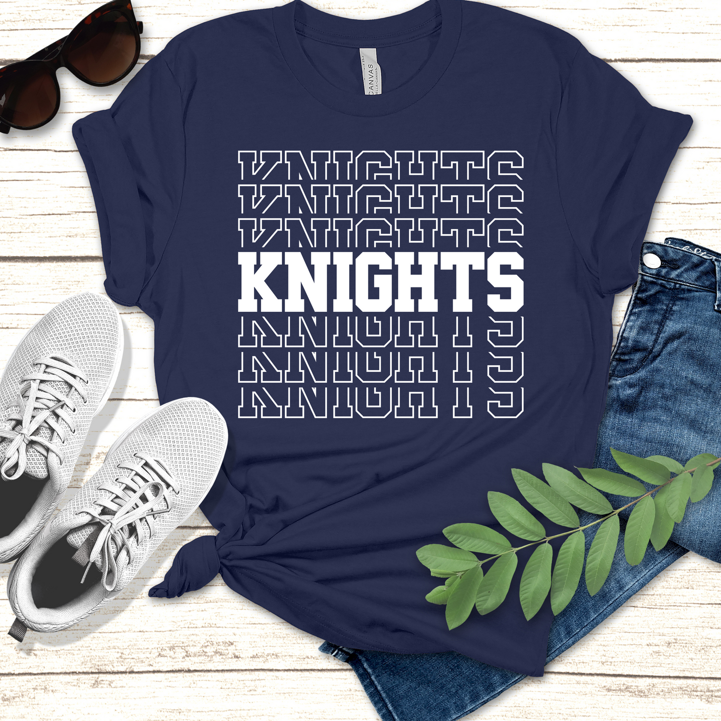 Navy blue t-shirt with 'KNIGHTS' text, paired with sneakers and jeans on a wooden surface. Knights School Spirit Shirt - Knights Stacked - Knights Spirit Tee
