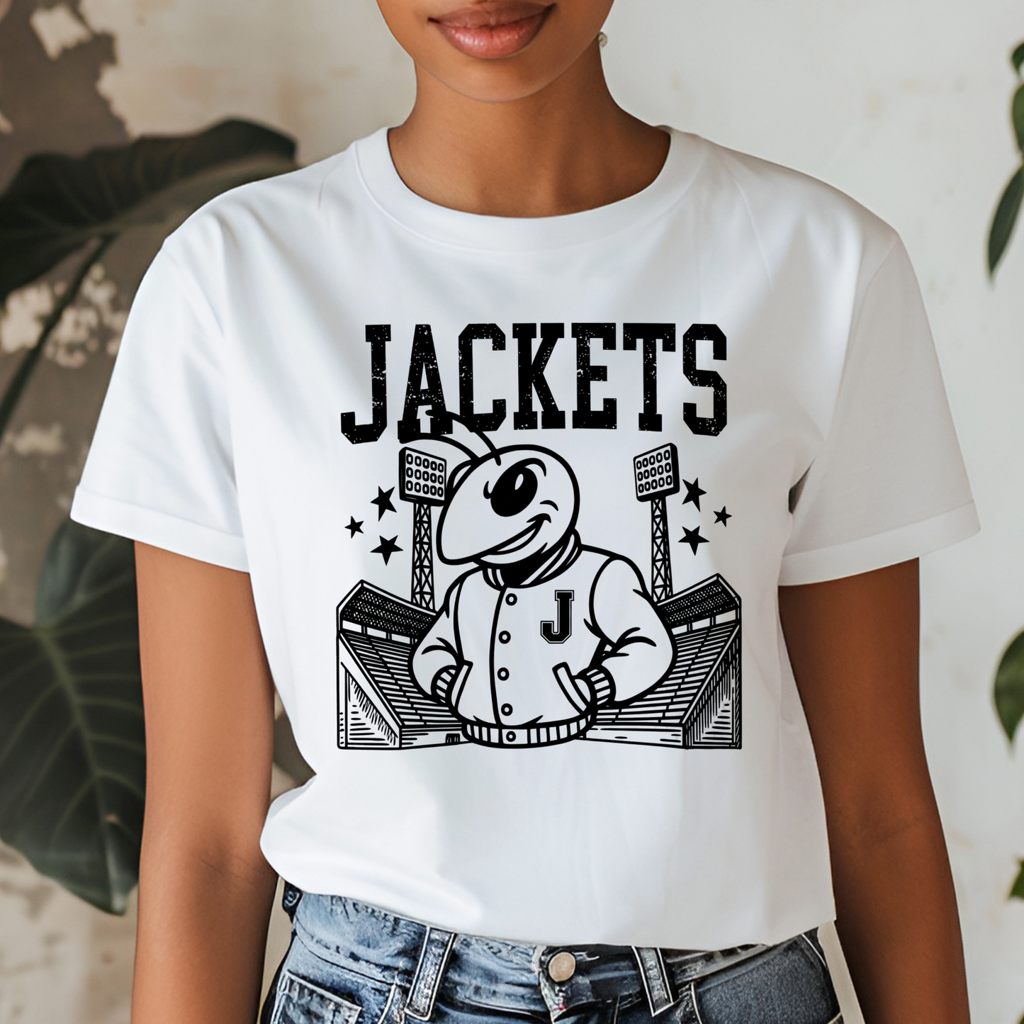 A person wearing a white short-sleeve T-shirt with a large black graphic print of a cartoon bee mascot in a baseball uniform and the word 'JACKETS' across the chest, paired with blue jeans.