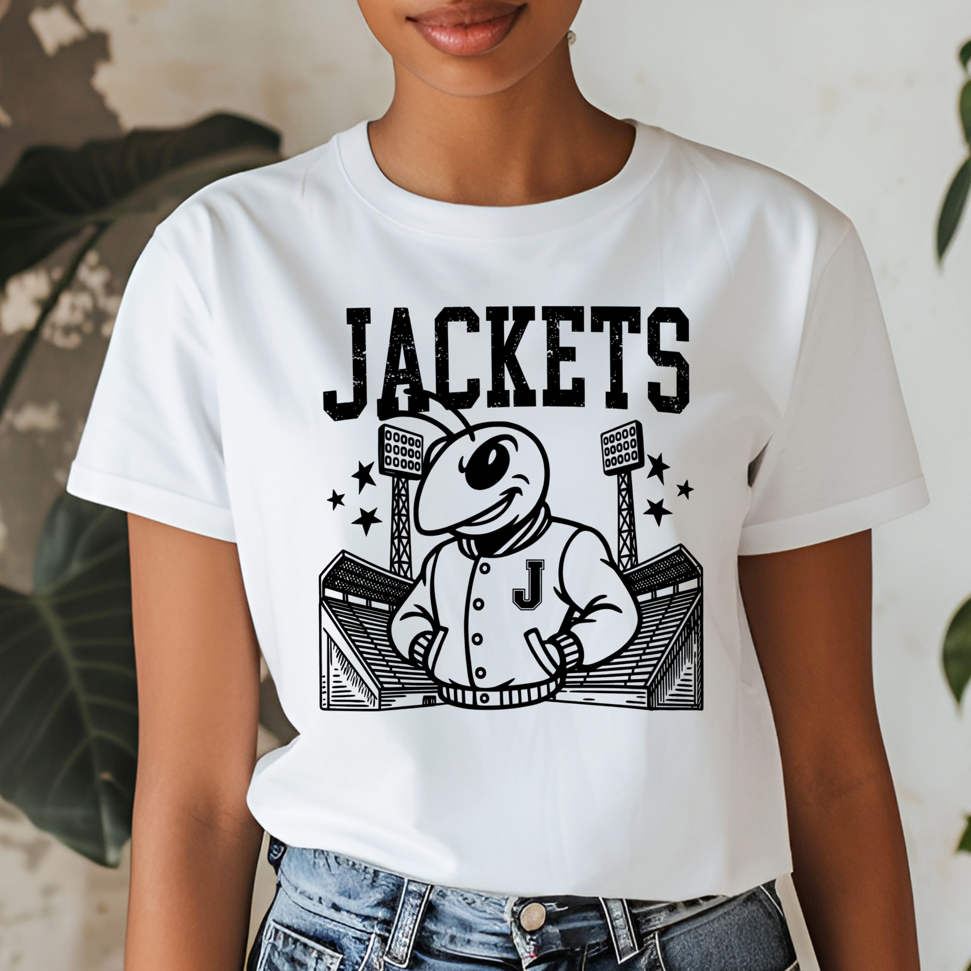 A person wearing a white short-sleeve T-shirt with a large black graphic print of a cartoon bee mascot in a baseball uniform and the word 'JACKETS' across the chest, paired with blue jeans.