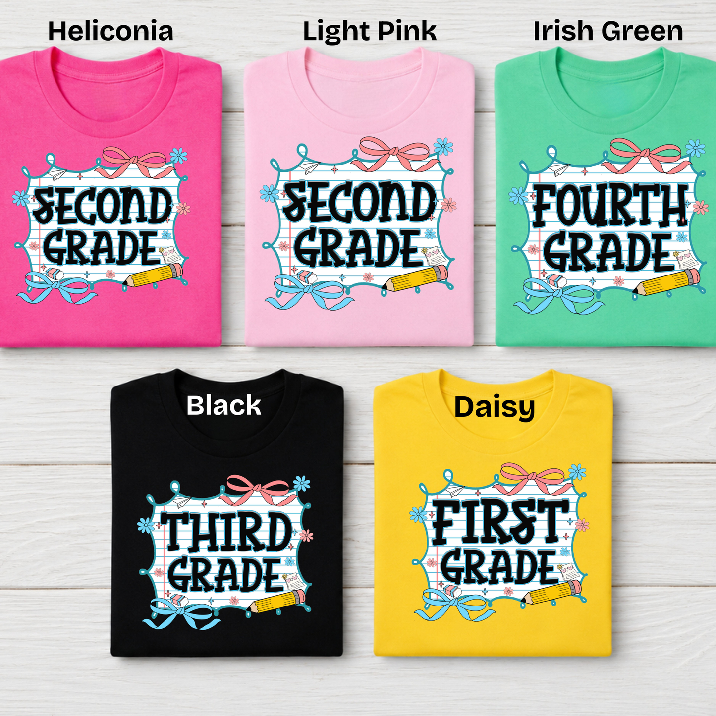 Five folded graphic T-shirts arranged in a 2x3 grid on a light wood background, labeled with color names at the top: Heliconia pink, Light Pink, Irish Green, Black, and Daisy yellow. Each shirt has a school-grade-themed graphic with text such as SECOND GRADE, FOURTH GRADE, THIRD GRADE, and FIRST GRADE.