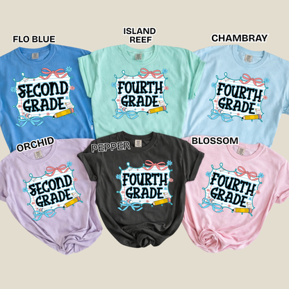 Six graphic t-shirts in different colors are arranged in a 2x3 grid on a beige background, each labeled with a color name: Flo Blue, Island Reef, Chambray, Orchid, Pepper, and Blossom. The shirts feature a colorful graphic design with the text 'SECOND/FOURTH GRADE' and decorative elements.