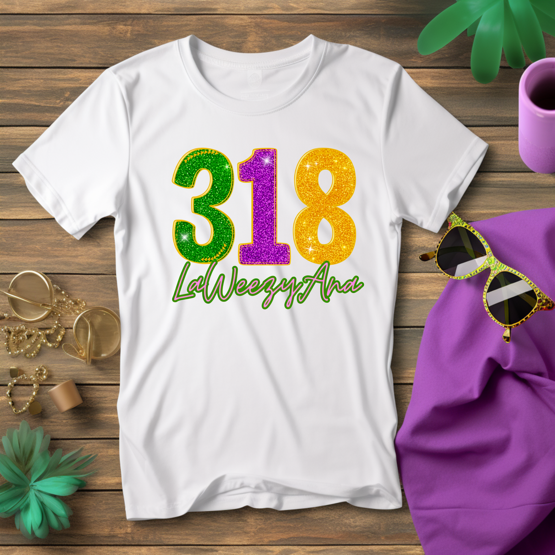 White t-shirt with colorful '318 LaWeezyAna' design on a wooden surface with sunglasses and a purple bag.