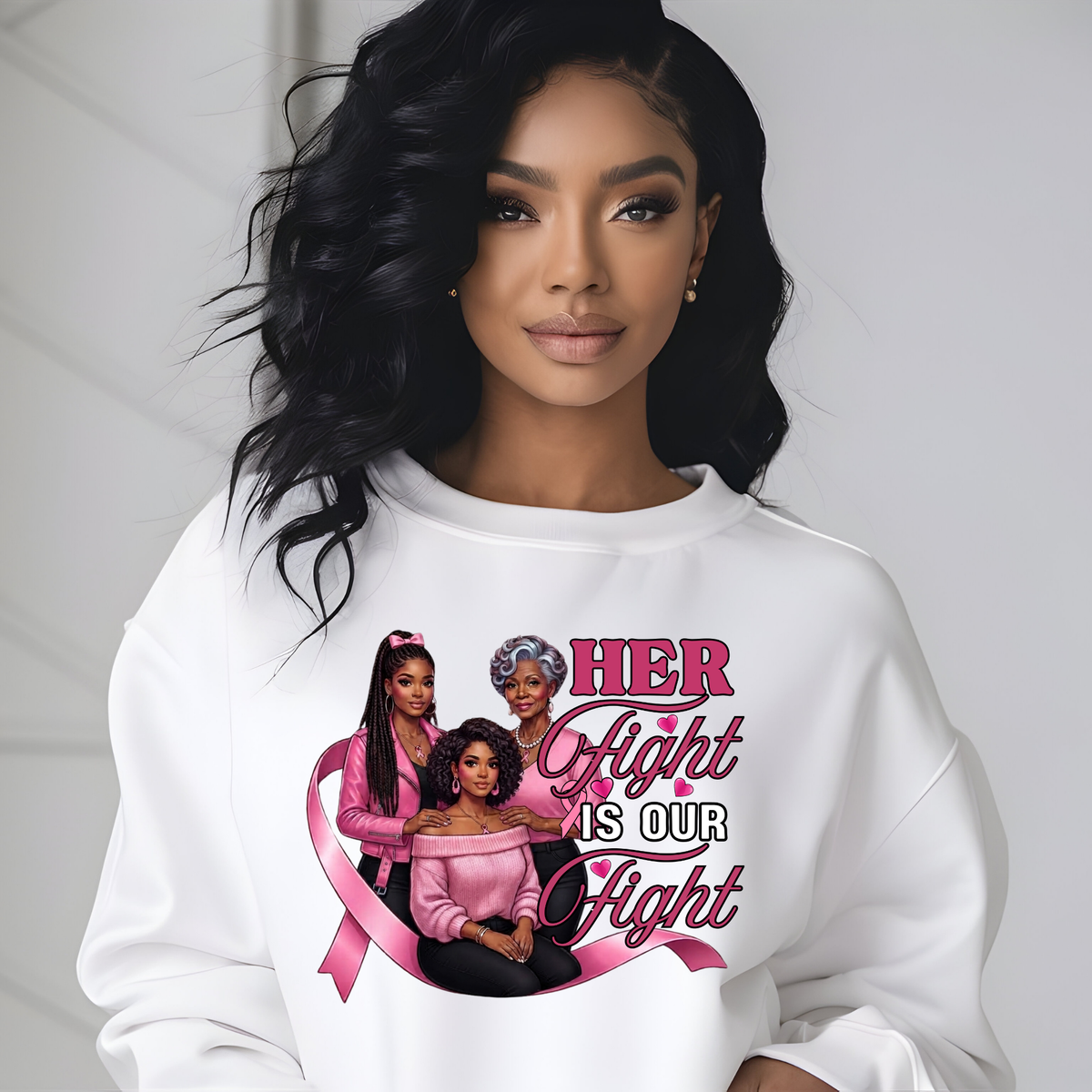 A woman wearing a white crewneck sweatshirt with a graphic print that reads 'HER Fight IS OUR Fight' in pink and black lettering, featuring three Black women and a pink ribbon. The background is a clean, light gray wall.